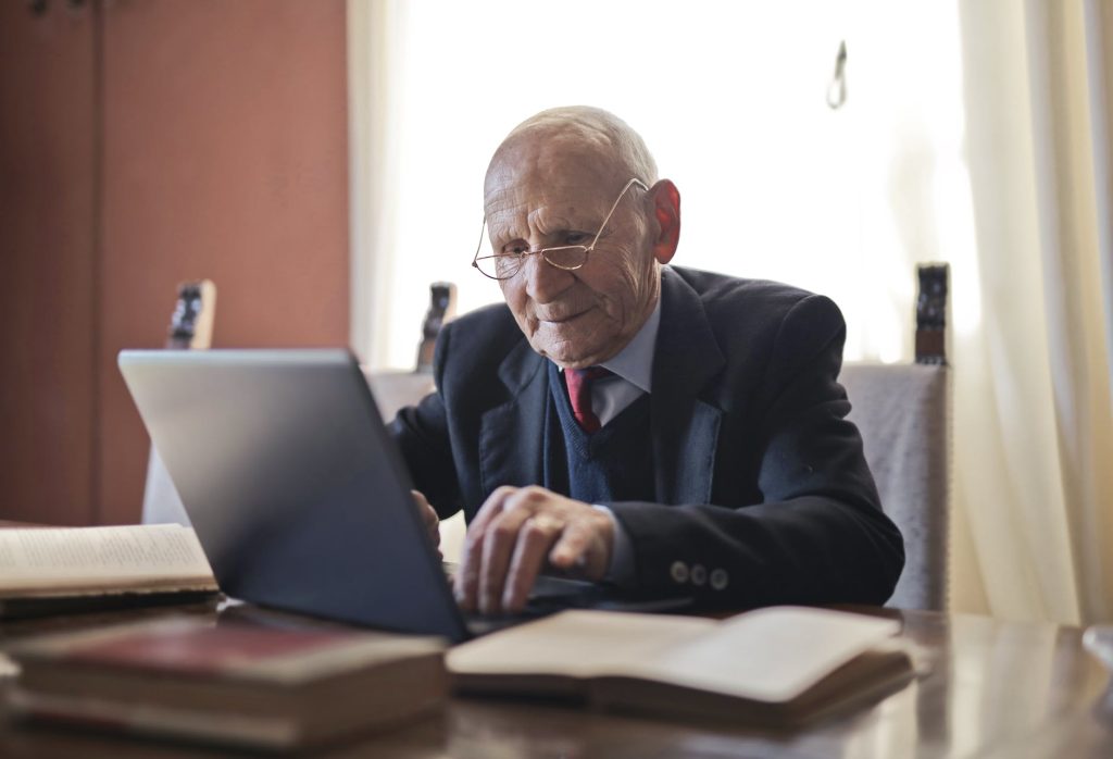 serious senior man using laptop while sitting at table with books, Teaching a senior how to use a computer 
