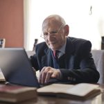 serious senior man using laptop while sitting at table with books